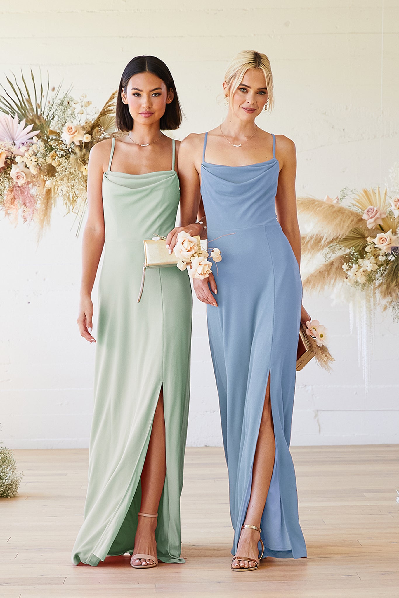 Front view of two slender models wearing Ash Bridesmaid Dresses, locking arms. The model on the left is in sage green and has a medium skin tone. The model on the right is in dusty blue and has a light skin tone. 