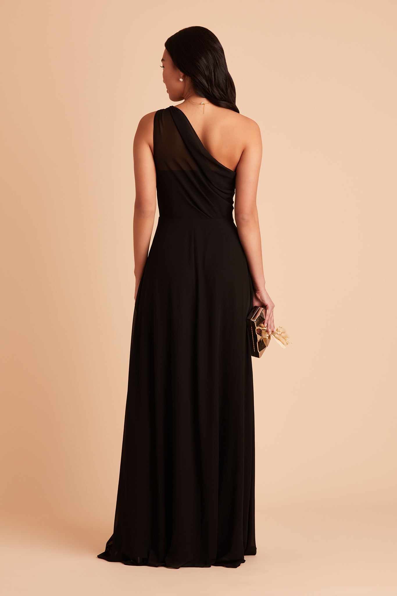 Back view of the Kira Dress in black chiffon shows the back of the dress with sheer chiffon fabric which creates a pleated Grecian one-shoulder neckline and bodice.