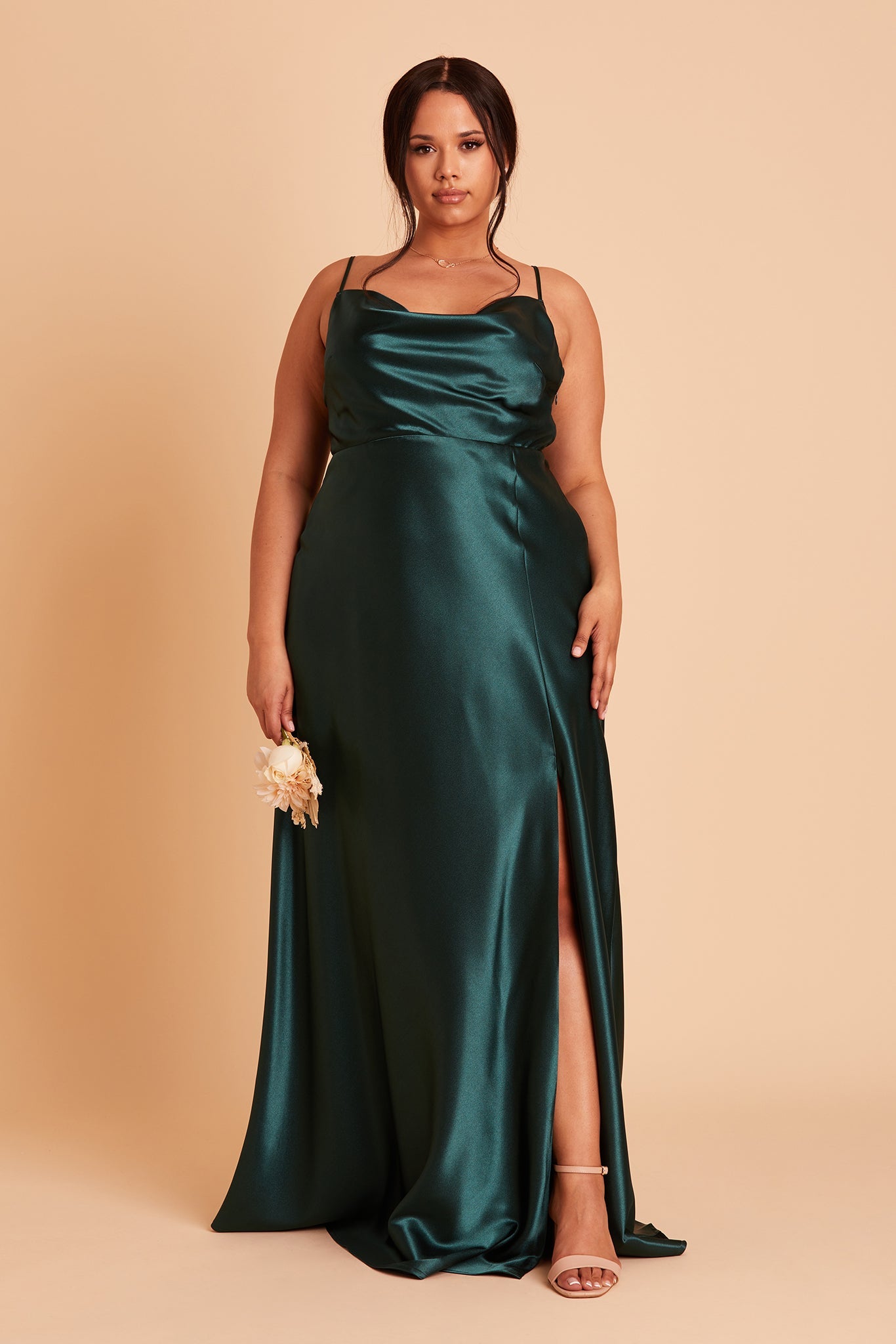 Front view of the Lisa Long Dress Curve in emerald satin shows a model revealing their leg and foot in the mid-thigh high slit. They wear the Natalie Chunky Heel shoe in nude blush.