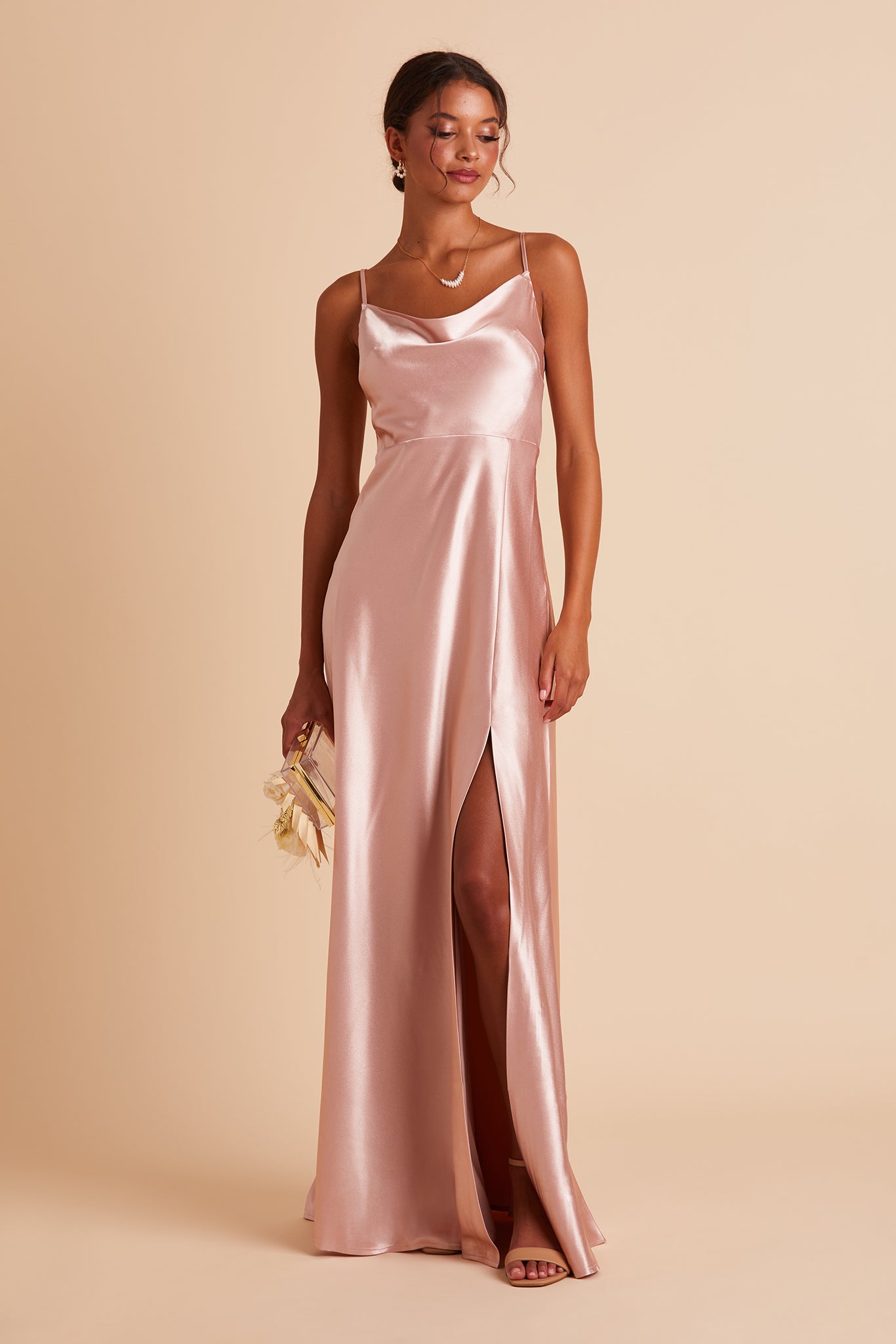 Front view of the Lisa Long Dress in rose gold satin shows a model revealing their leg and foot in the mid-thigh high slit. They wear the Mary Chunky High Heel shoe in nude latte.