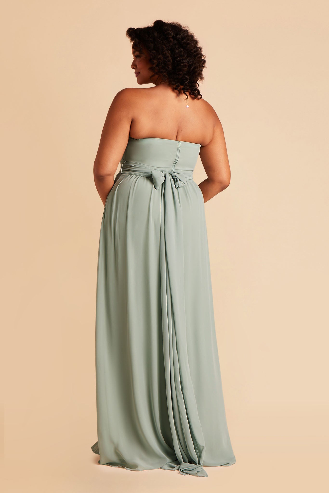 Back view of the Grace Convertible Plus Size Bridesmaid Dress in sage chiffon reveals an open back cut below the shoulder blades with front streamers tied around the waist in a delicate and flowing bow.