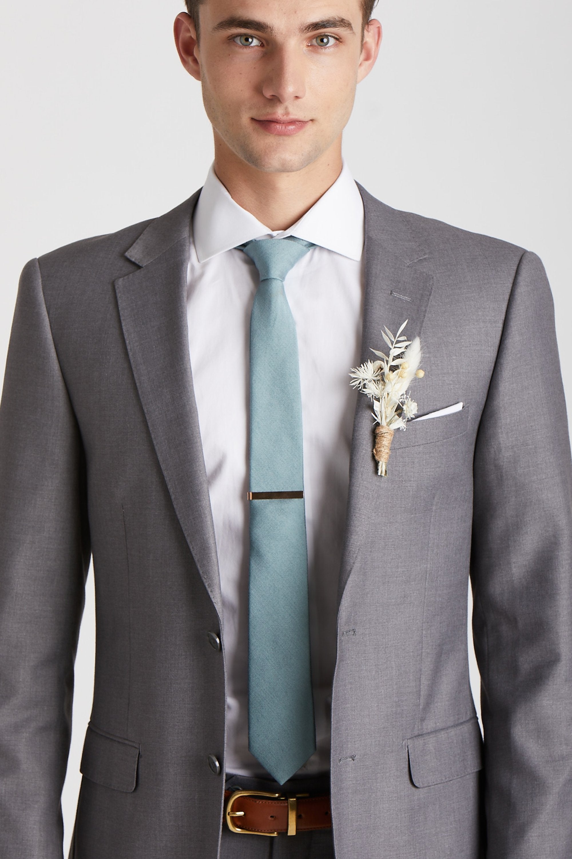 Front closeup view of the model wearing the Simon Necktie in sea glass with a white button down collared shirt and medium grey suit. The tie is kept in place with a narrow rectangular necktie clasp in gold.