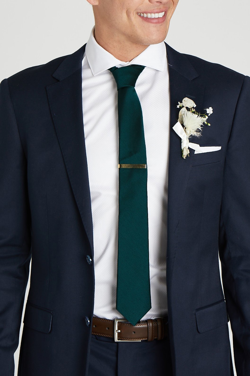 Front closeup view of the model wearing the Simon Necktie in emerald with a white button down collared shirt and navy blue suit. The tie is kept in place with a narrow rectangular tie clasp in matte gold.