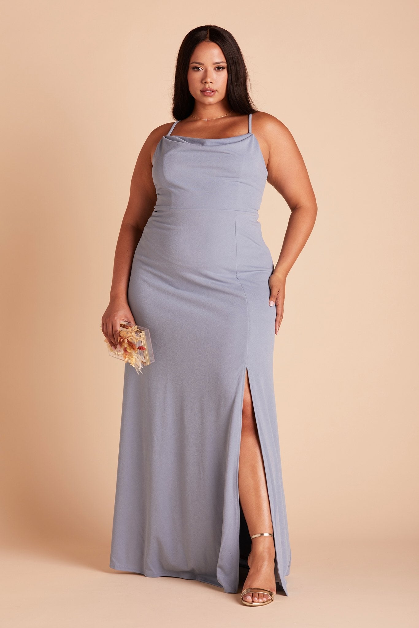 Front view of the floor-length Ash Plus Size Bridesmaid Dress in dusty blue crepe by Birdy Grey with a slightly draped cowl neck front. The flowing skirt features a slit over the front left leg.