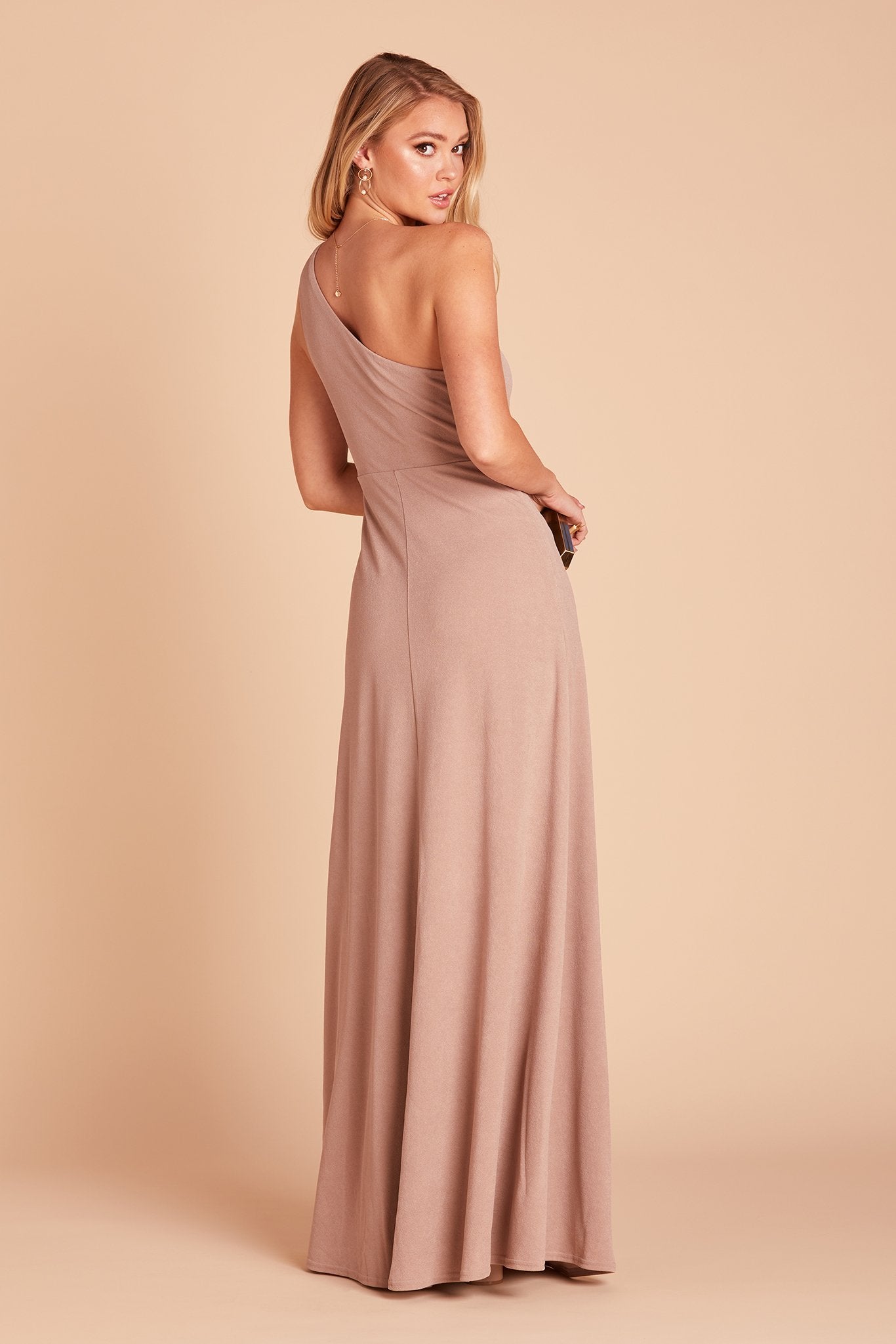 Back and side view of the Kira Dress in taupe crepe shows a slender model with a light skin tone looking backwards over their shoulder demonstrating the drape and fit of the off-the-shoulder bodice and flowing skirt.