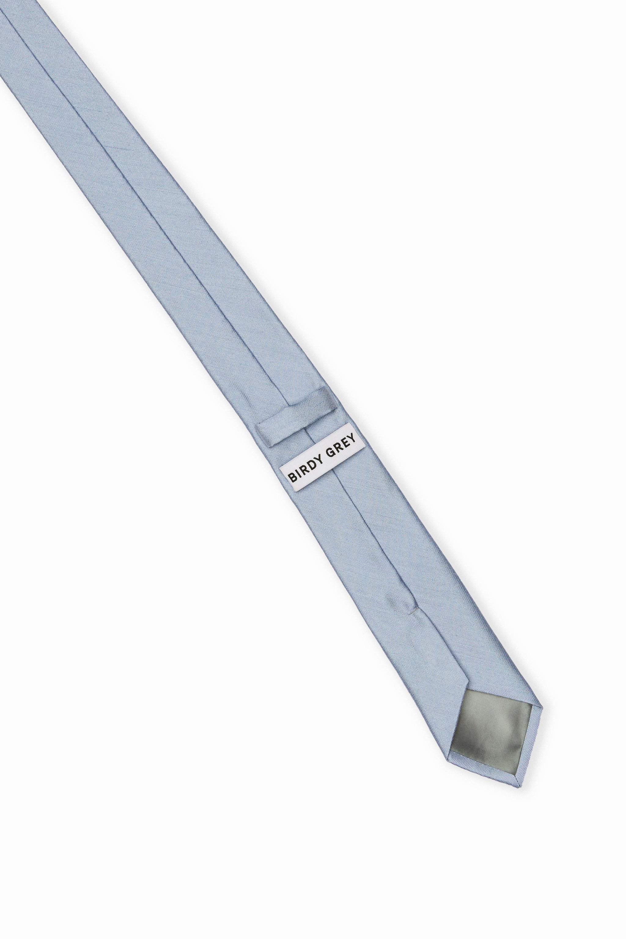 Elevated back view of the Simon Necktie in dusty blue fully extended on a white background showing the necktie satin lining in light grey, a keeper loop to tuck the necktie end, and a label that reads, 