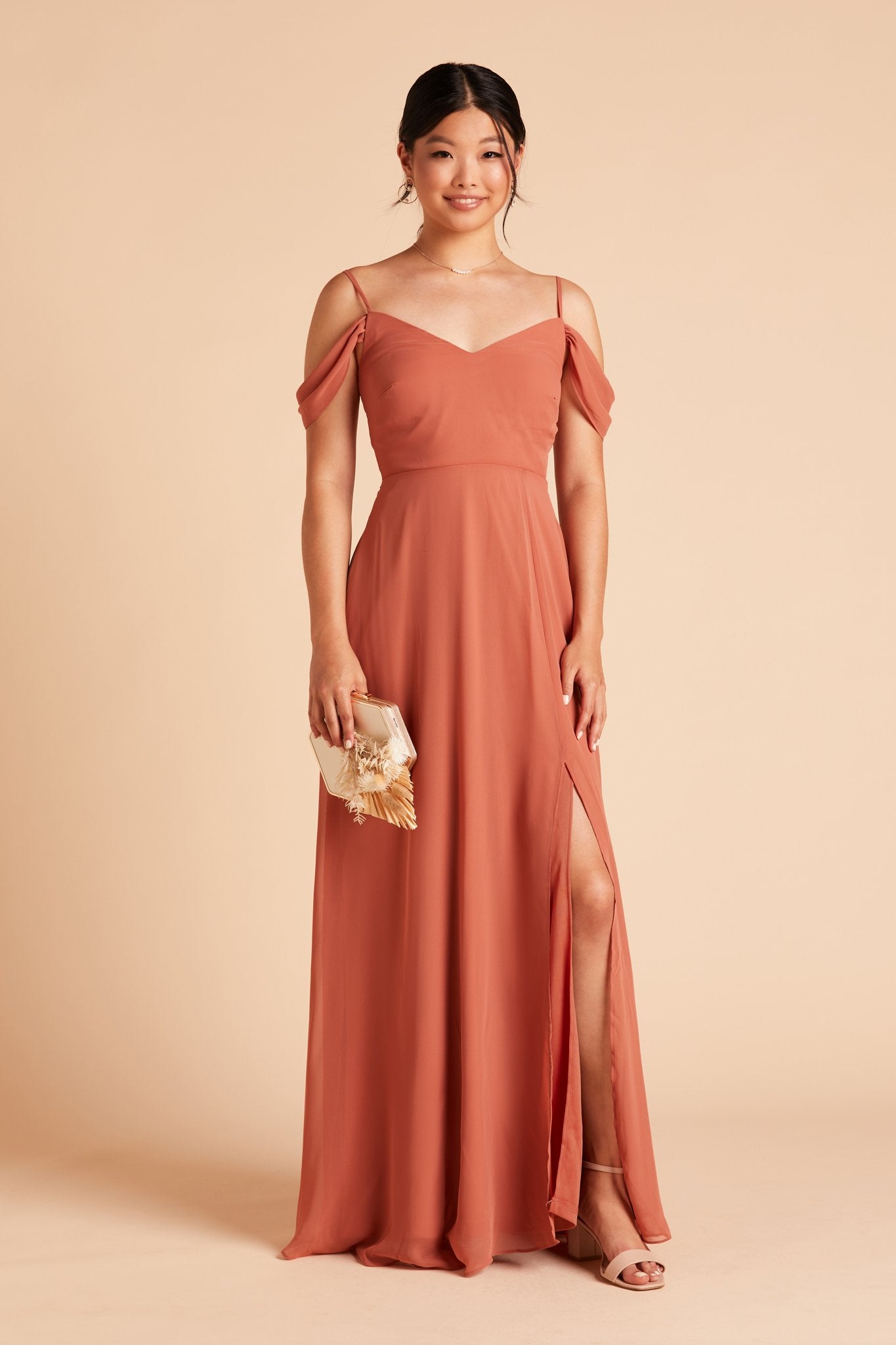 Front view of the floor-length Devin Convertible Bridesmaid Dress in terracotta chiffon by Birdy Grey with a V-neck front and draping detachable sleeves. The dress features an optional slit over the left front leg.
