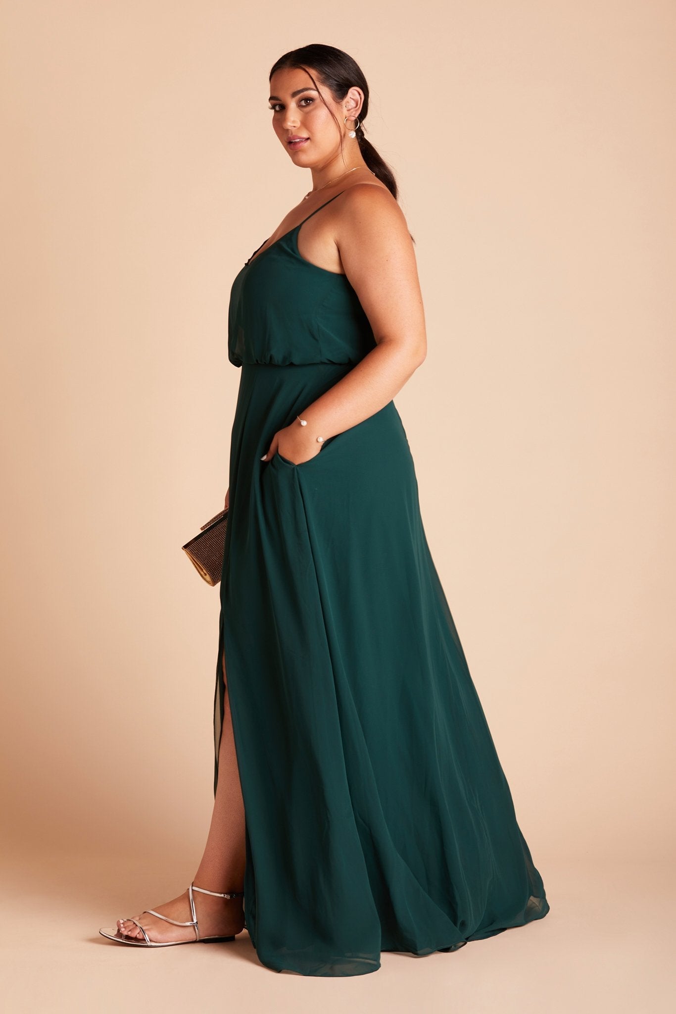 Gwennie plus size bridesmaid dress with slit in emerald green chiffon by Birdy Grey, side view with hand in pocket