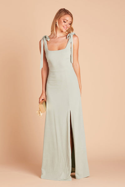 Front view of the Alex Convertible Bridesmaid Dress in crepe sage by Birdy Grey. The dress has a slit over the front left leg and shoulder ties tied in a bow and draped down over each shoulder. 