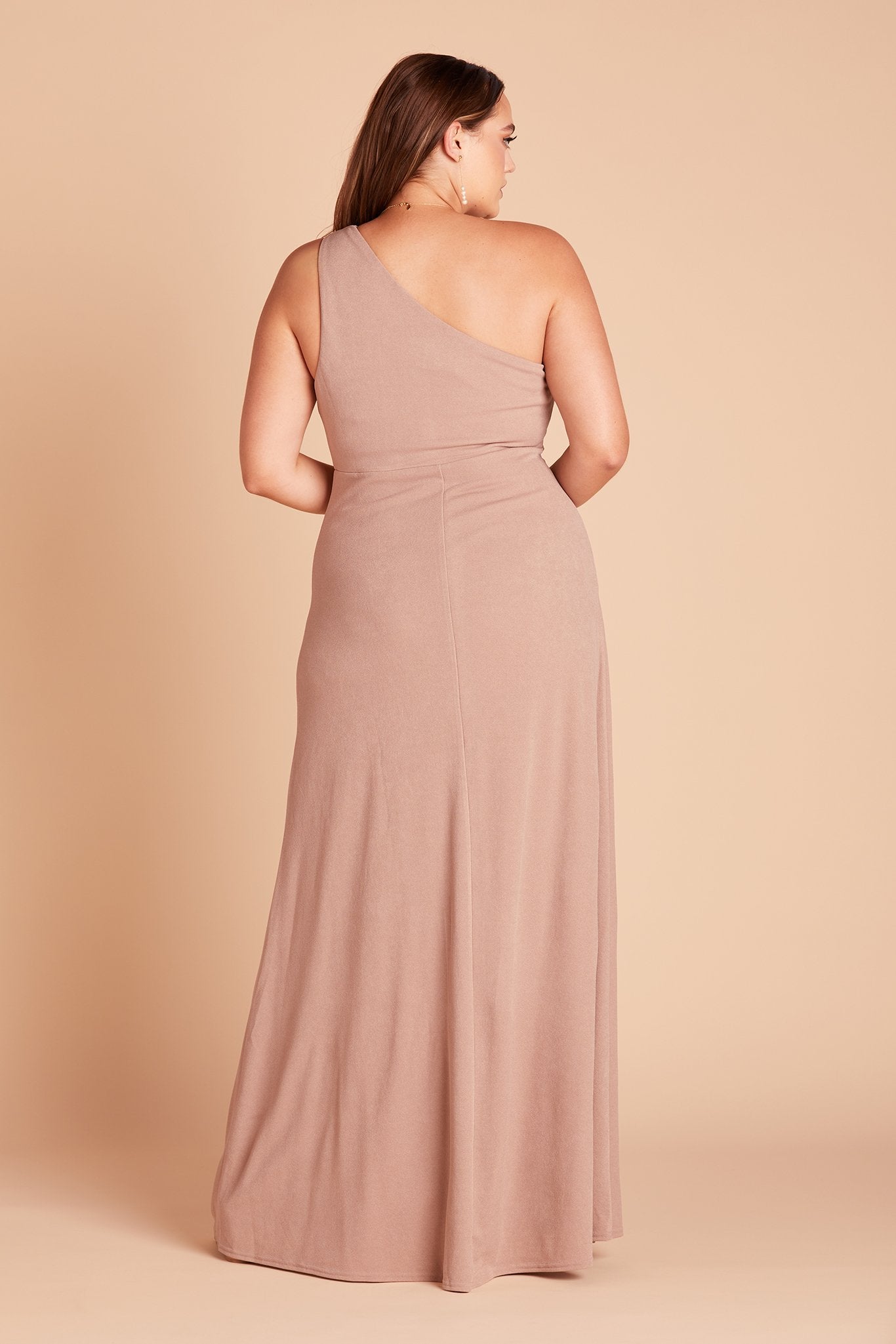 Back view of the Kira Dress Curve in taupe crepe shows a model with their back to us showing the body conforming fit of the bodice, waist, and hips and the flow of the dress skirt. 