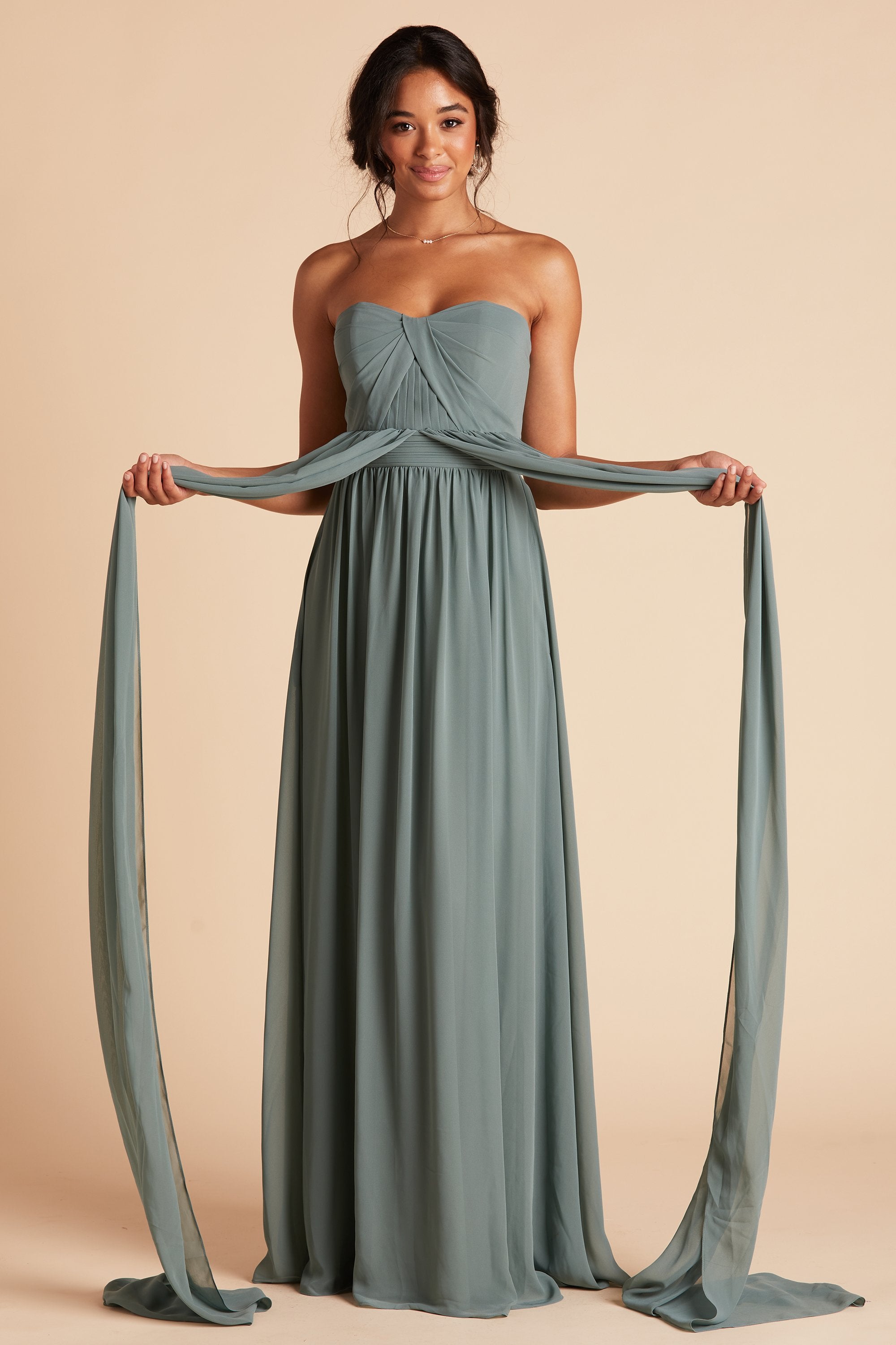 Front view of the Grace Convertible Bridesmaid Dress in sea glass chiffon as the model holds a front streamer connected at the waist in each hand. The streamers are extra long, longer than the floor-length skirt.