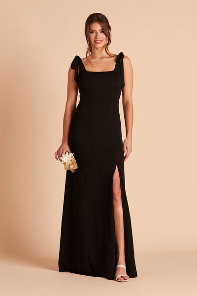 Front view of the Alex Convertible Bridesmaid Dress in black crepe by Birdy Grey. The dress has a slit over the front left leg and shoulder ties tied in a bow and draped down over each shoulder. 