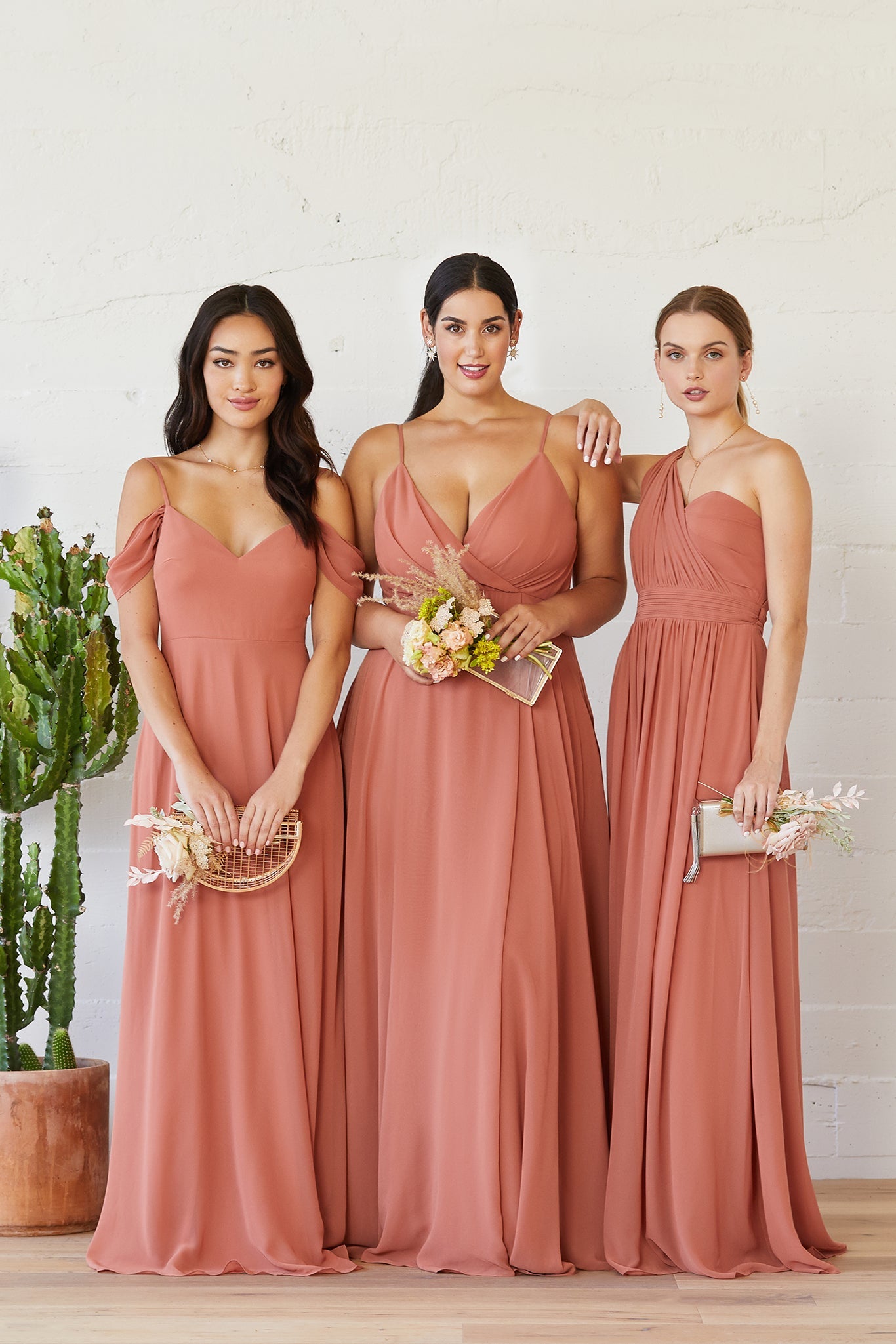 Front view shows three models with a light skin tone in different full-length dresses in terracotta. A slender model wears the Devon Convertible Dress. A full-figured model wears the Kaia Dress Curve. A slender model wears the Grace Convertible Dress. 