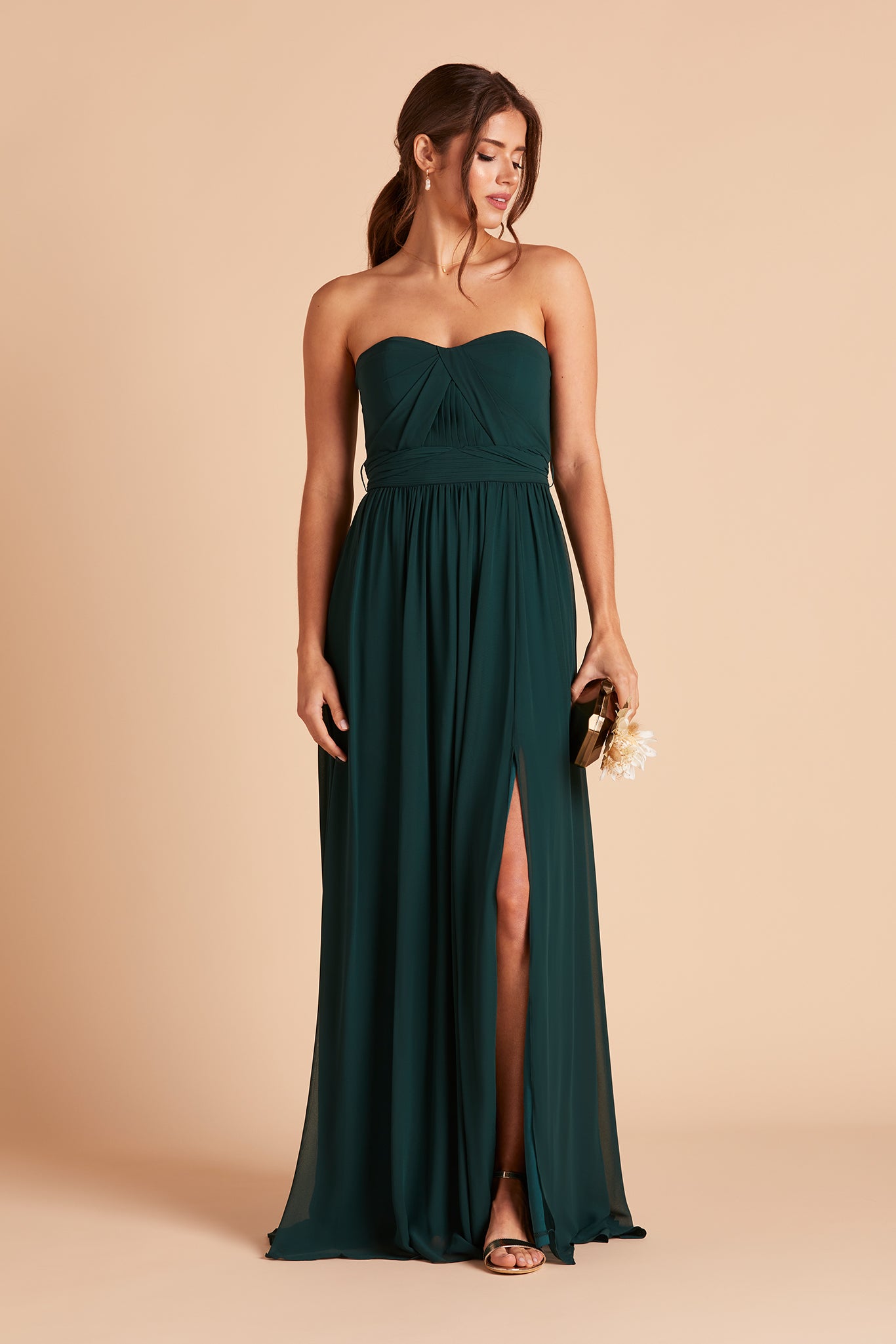 Front view of the Grace Convertible Bridesmaid Dress in emerald chiffon worn by a slender model with a light skin tone. Front streamers are pulled back and tied behind the waist. 