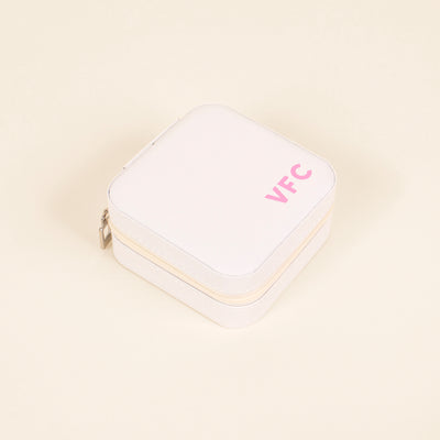 Elevated view of the White Jewelry Box showing a soft faux leather top monogrammed with the initials VFC in rose pink. The box has a rounded square shape and a white zipper with a silver pull running along the middle of the box. 