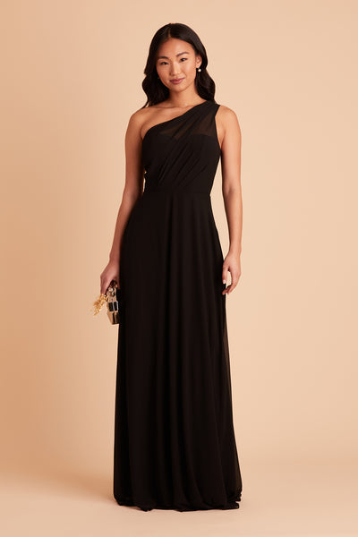 Front view of the Kira Dress in black chiffon shows a slender model wearing an asymmetrical one-shoulder, full-length dress. Chiffon gathers into soft pleating at the shoulder of the bodice with a smooth fit at the waist as the dress skirt with a slight A-line silhouette flows to the floor.    
