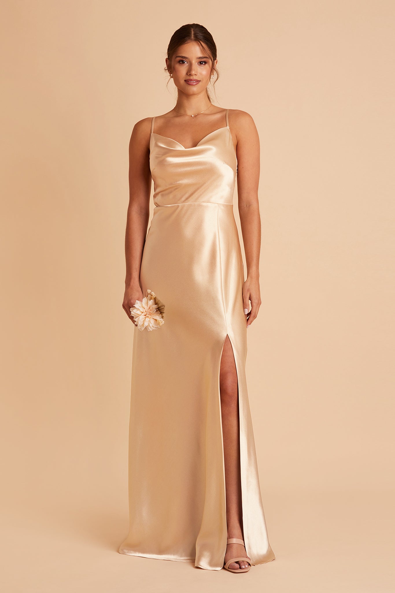 Front view of the Lisa Long Dress in gold satin shows a model with their left leg and foot revealed through a mid-thigh high dress slit. They wear the Natalie Chunky Heel shoes in nude blush.