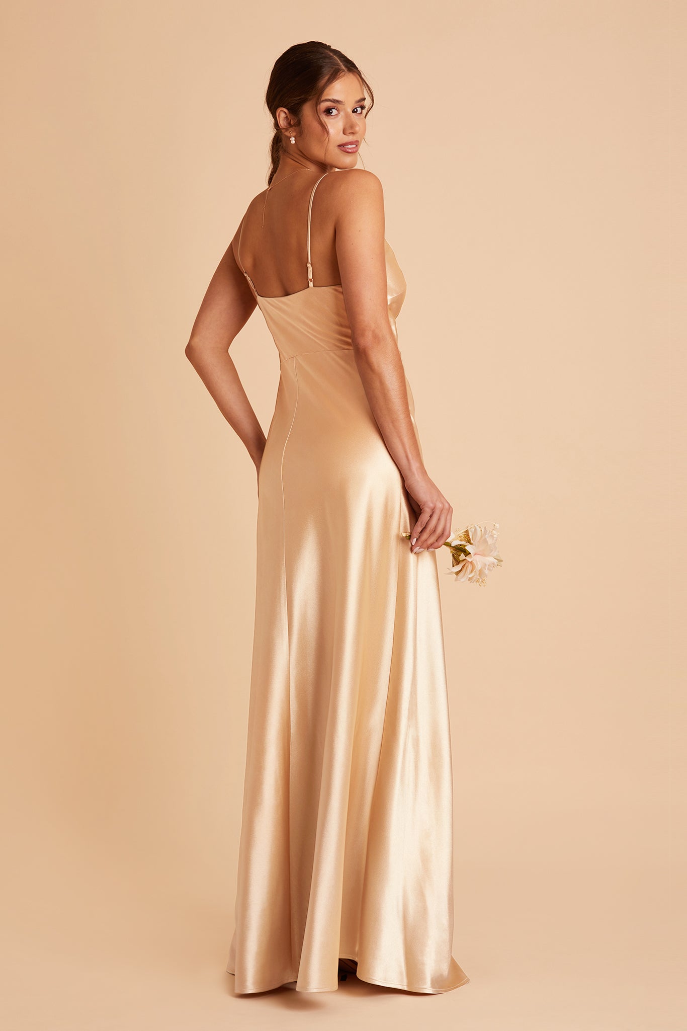 Back view of the Lisa Long Dress in gold satin shows the back of the dress with adjustable spaghetti straps and a smooth fit in the bodice and waist that attach to a floor-length skirt.  