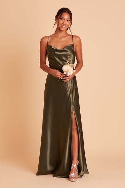 Front view of the Lisa Long Dress in olive satin shows a slender model with a medium skin tone wearing a lightly draped cowl neck bodice with spaghetti straps and a floor length flared dress with a slit. 
