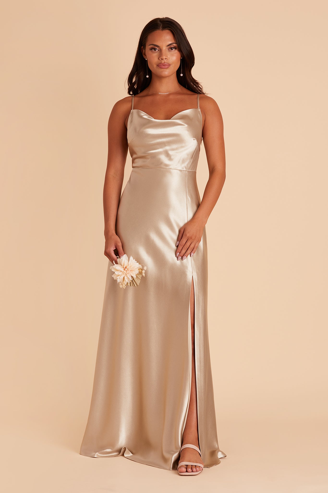 Front view of the Lisa Long Dress in neutral champagne satin shows a model revealing their leg and foot in the mid-thigh slit. They wear the Natalie Chunky Heel shoes in nude blush.