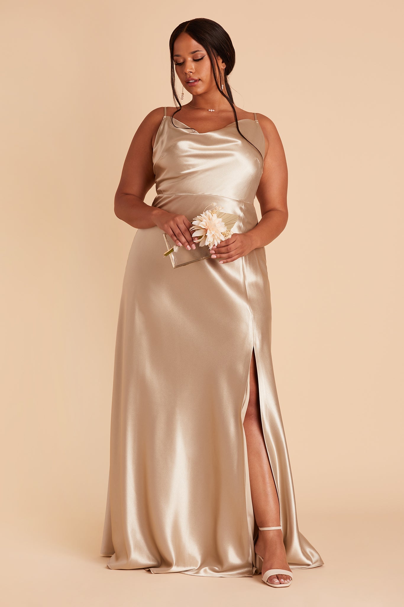 Front view of the Lisa Long Dress Curve in neutral champagne satin shows a model revealing their leg and foot in the mid-thigh high slit. They wear the Natalie Chunky Heel shoe and the Durham Pearl Trio Necklace. 