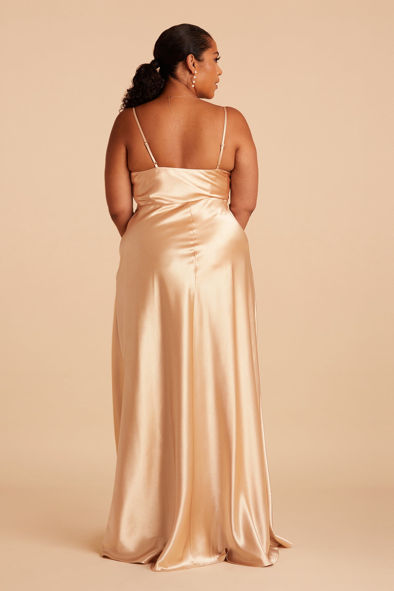 Back view of the Lisa Long Dress Curve in gold satin shows the back of the dress with adjustable spaghetti straps and a smooth fit in the bodice and waist that attach to a full length skirt.  