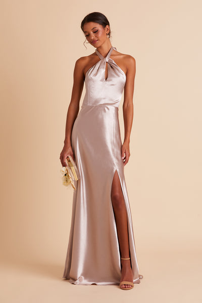 Front view of the Monica Dress in taupe satin shows a slender model with a medium skin tone wearing an A-line full length dress with a left slit. The Grecian twist front halter with tie back conforms to the bosom and waist with a smooth fit at the dress skirt top. 