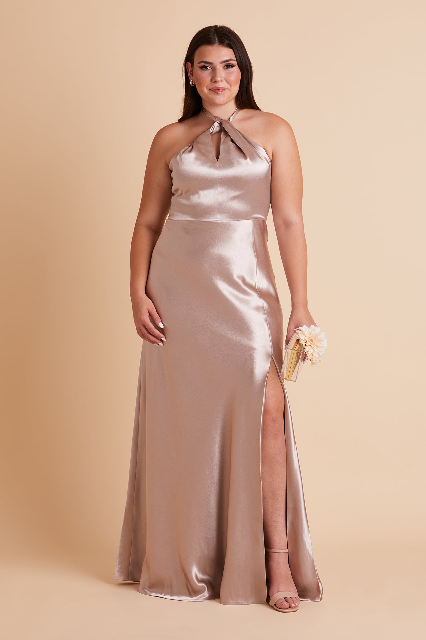 Front view of the Monica Dress Curve in taupe satin shows the model revealing their leg and foot through the dress slit. The model wears the Natalie Chunky Heel in almond.