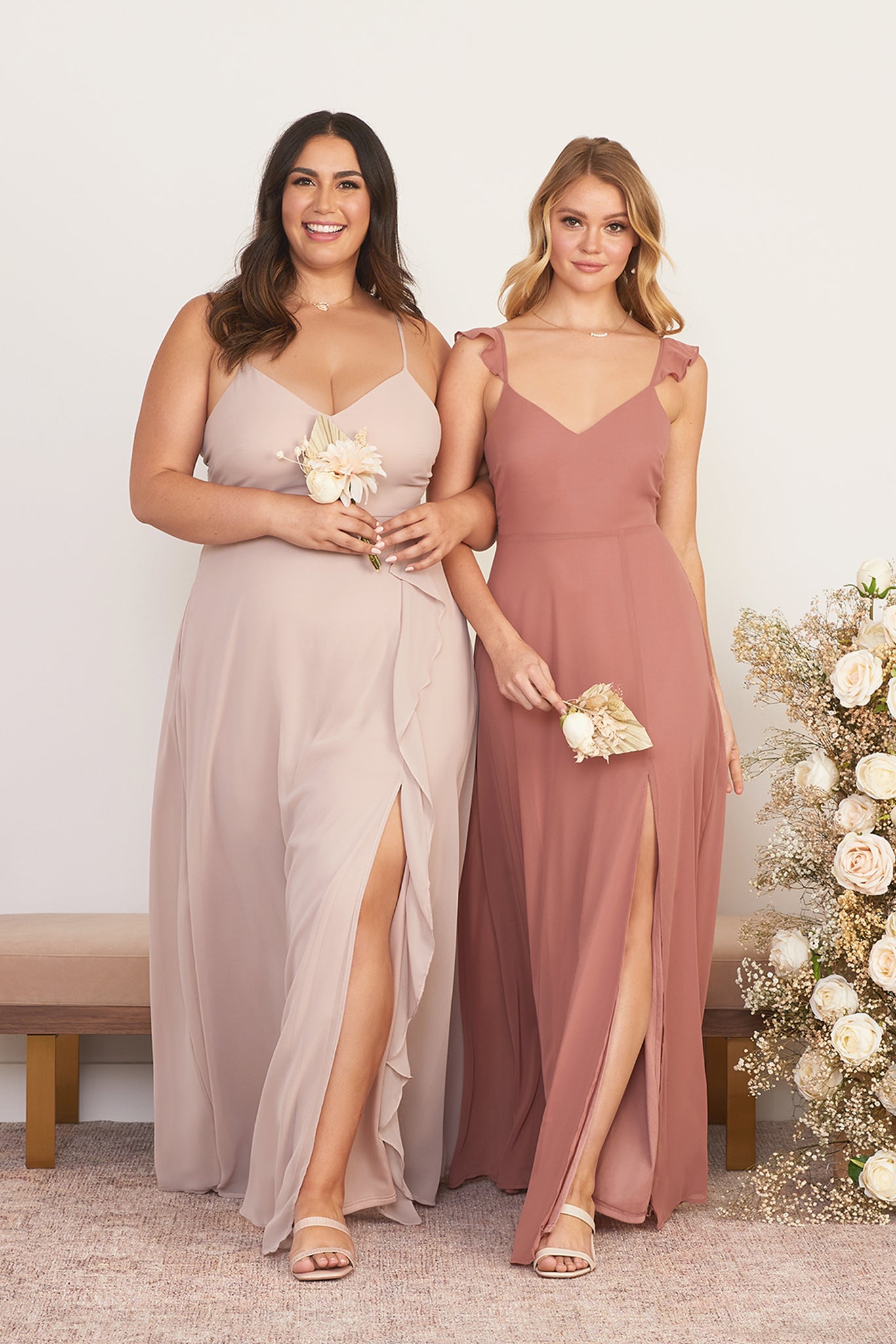Front view of two models wearing coordinating floor length dresses with slits. The Theresa Dress Curve is worn by full figured model with a light skin tone in taupe chiffon. The second dress is worn by a slender model with a light skin tone in desert rose. 