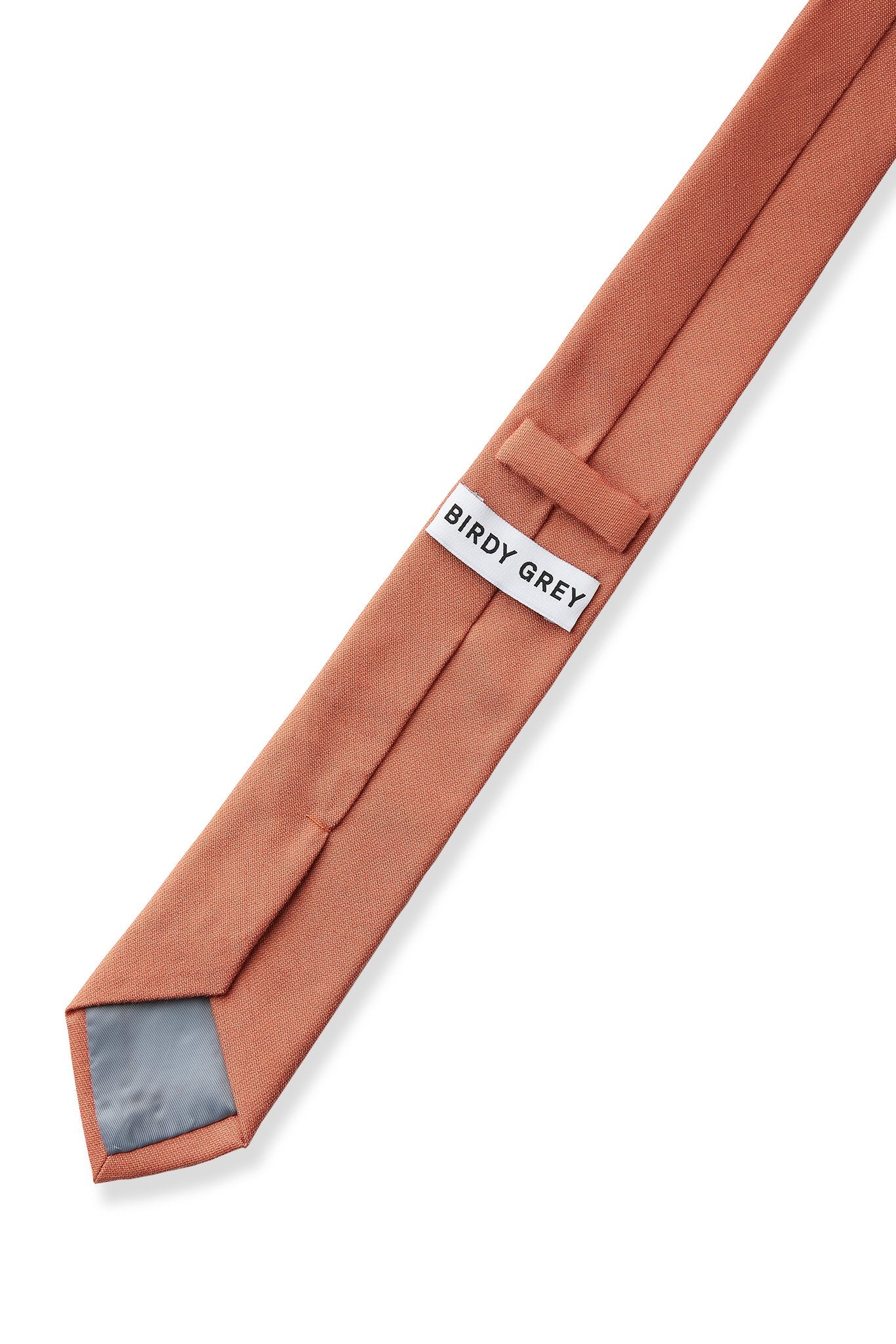 Elevated back view of the Simon Necktie in terracotta fully extended on a white background showing the necktie satin lining in grey, a keeper loop to tuck the necktie end, and a label that reads, 