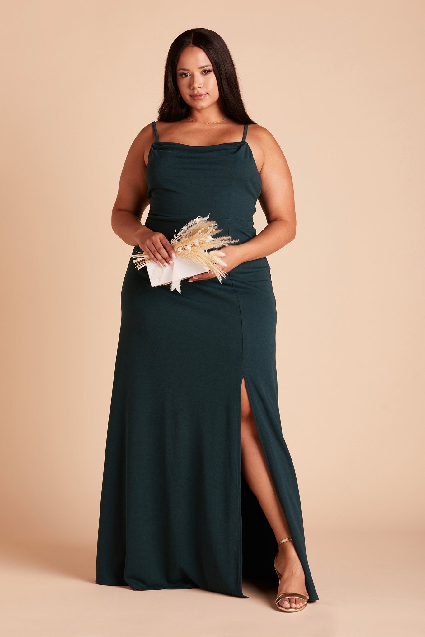 Front view of the floor-length Ash Plus Size Bridesmaid Dress in emerald crepe by Birdy Grey with a slightly draped cowl neck front. The flowing skirt features a slit over the front left leg.