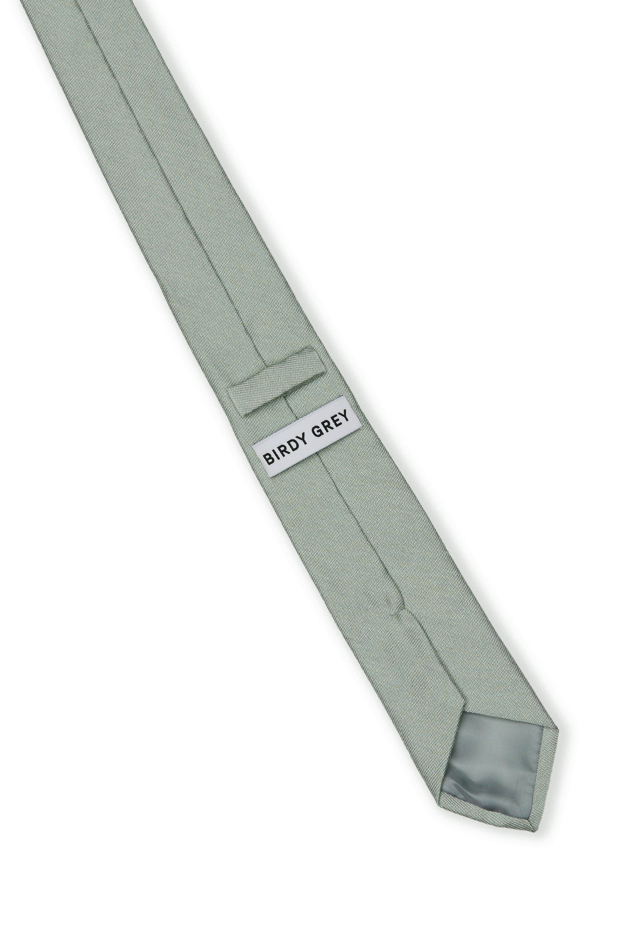 Elevated view of the Simon Necktie in sage fully extended on a white background showing the back of the necktie with grey satin lining, a keeper loop to tuck the necktie end, and a label that reads, 