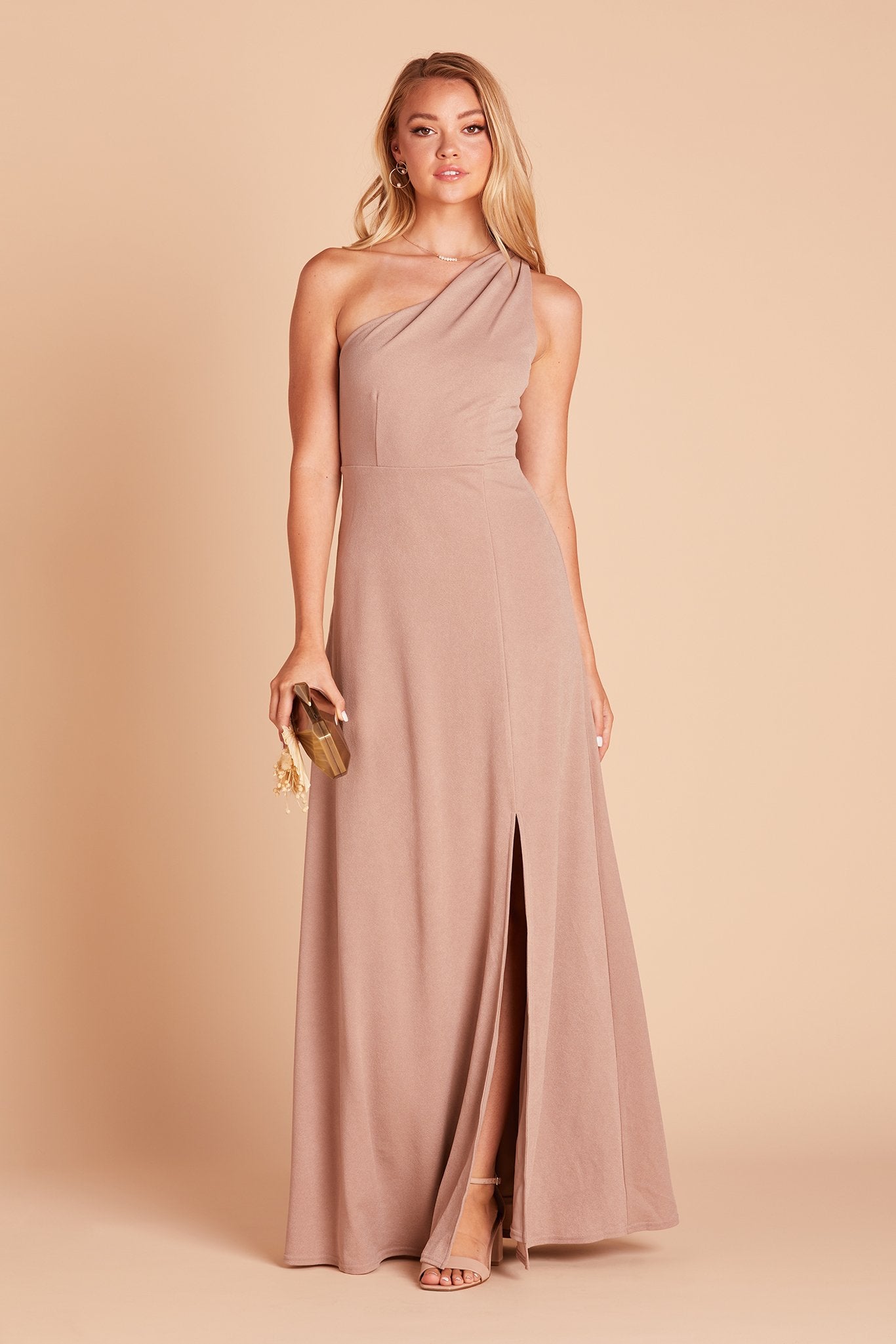 Front view of the Kira Dress in taupe crepe shows a model looking at us as they step forward revealing their lower leg. They wear the Mary High Curve Heel shoe in nude blush. 