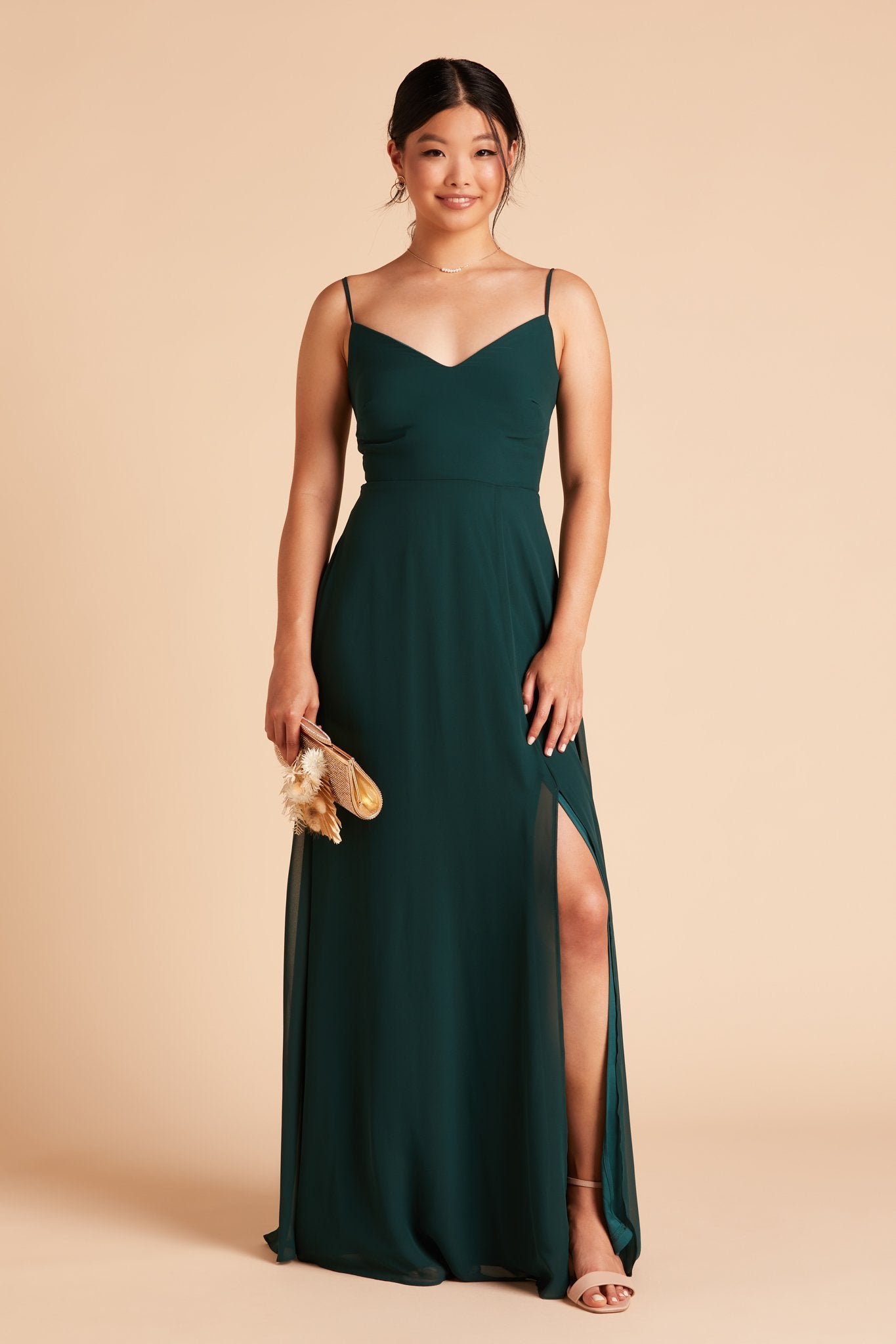 Front view of the floor length Devin Convertible Bridesmaid Dress in emerald with a flowing skirt features the optional slit over the front left leg.