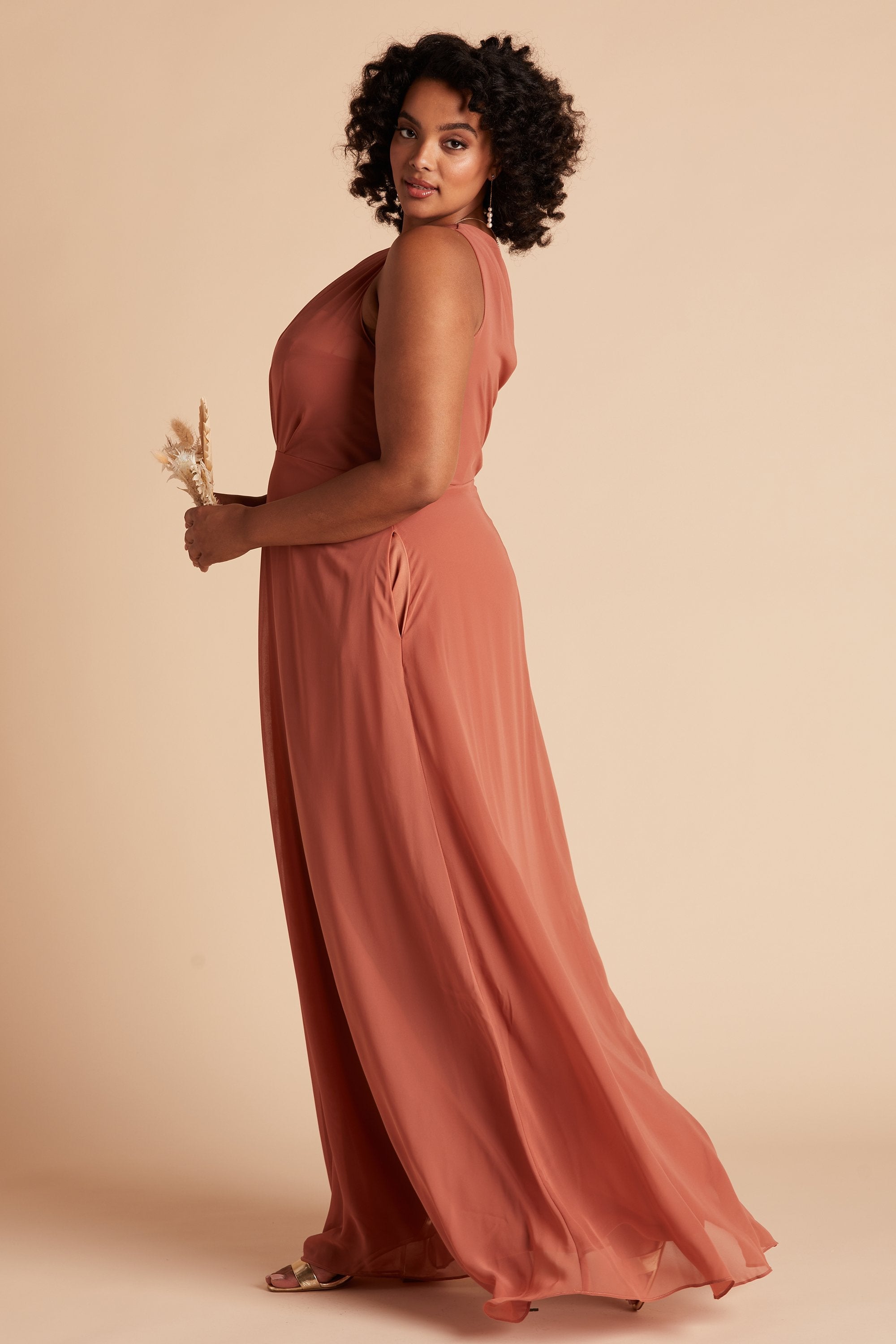 Side view of the Kira Dress Curve in terracotta chiffon shows a full-figured model with a medium skin tone and the side inseam dress pocket. 