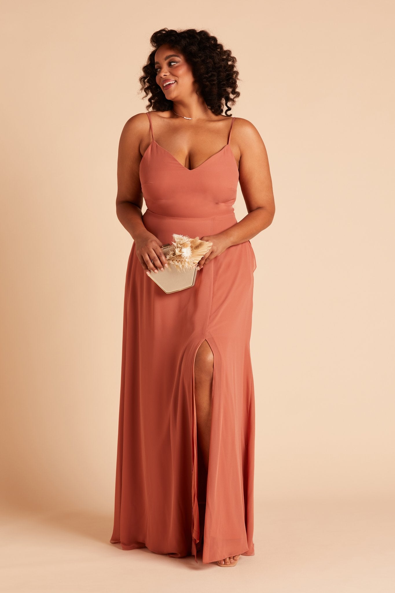 Front view of the floor-length Devin Convertible Plus Size Bridesmaid Dress in terracotta chiffon by Birdy Grey with a V-neck front and spaghetti straps. The dress features an optional slit over the left front leg.