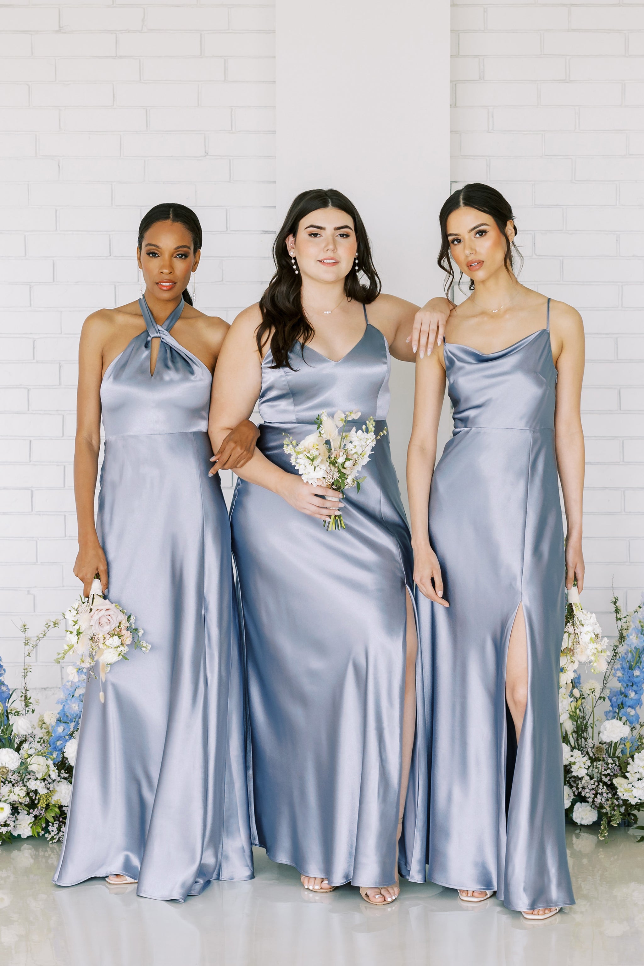 Three models wearing dusty blue satin dresses