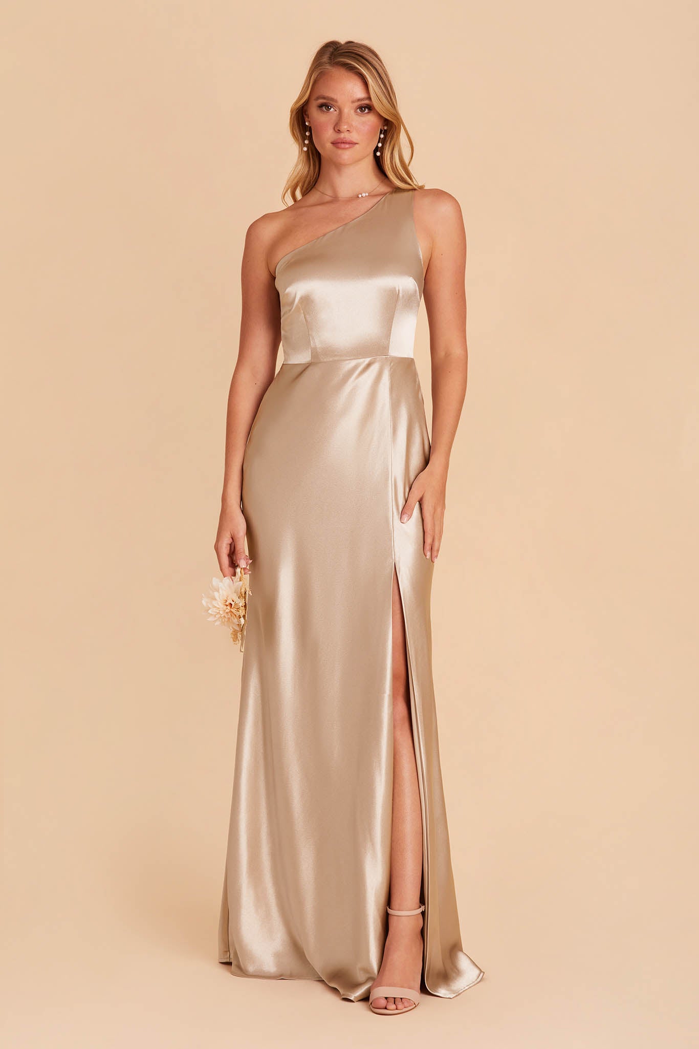 Front view of the Kira Dress in neutral champagne satin with a slit shows a slender model with a light skin tone wearing the Brookhaven Trio Pearl Necklace with Lowell Pearl Drop Earrings. The mid-thigh slit reveals their leg and the Natalie Chunky Heel shoes in nude blush.