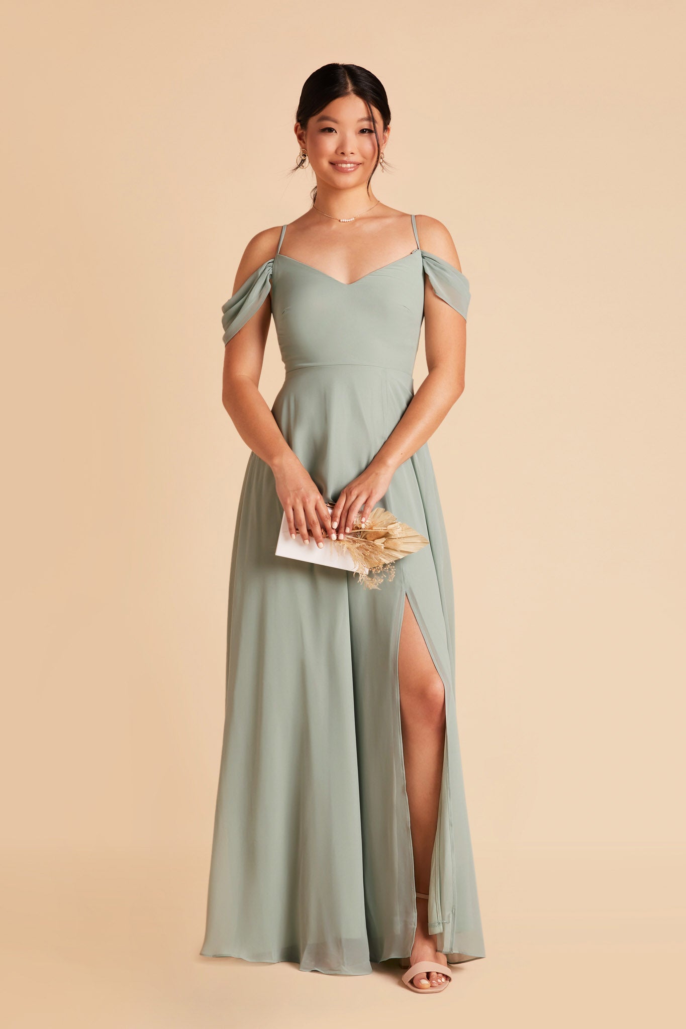 Front view of the floor-length Devin Convertible Bridesmaid Dress in sage chiffon by Birdy Grey with a V-neck front and draping detachable sleeves. The flowing skirt features a slit over the left leg.