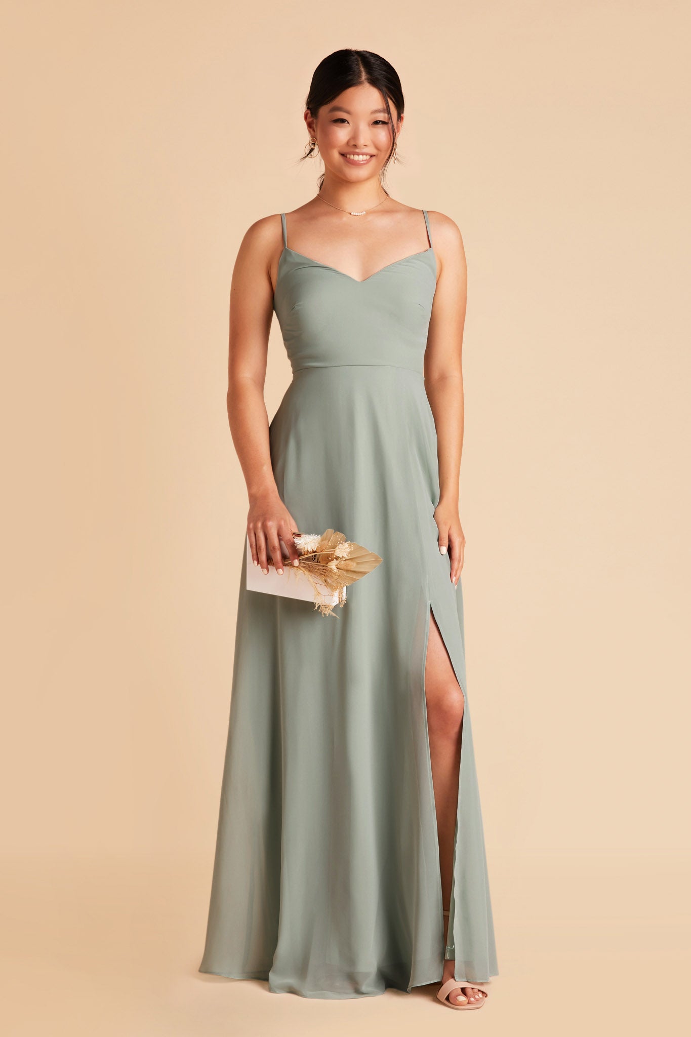 Front view of the floor-length Devin Convertible Bridesmaid Dress in sage chiffon worn by a slender model with a medium skin tone. The model wears the dress without the sleeves, with a simple spaghetti strap.