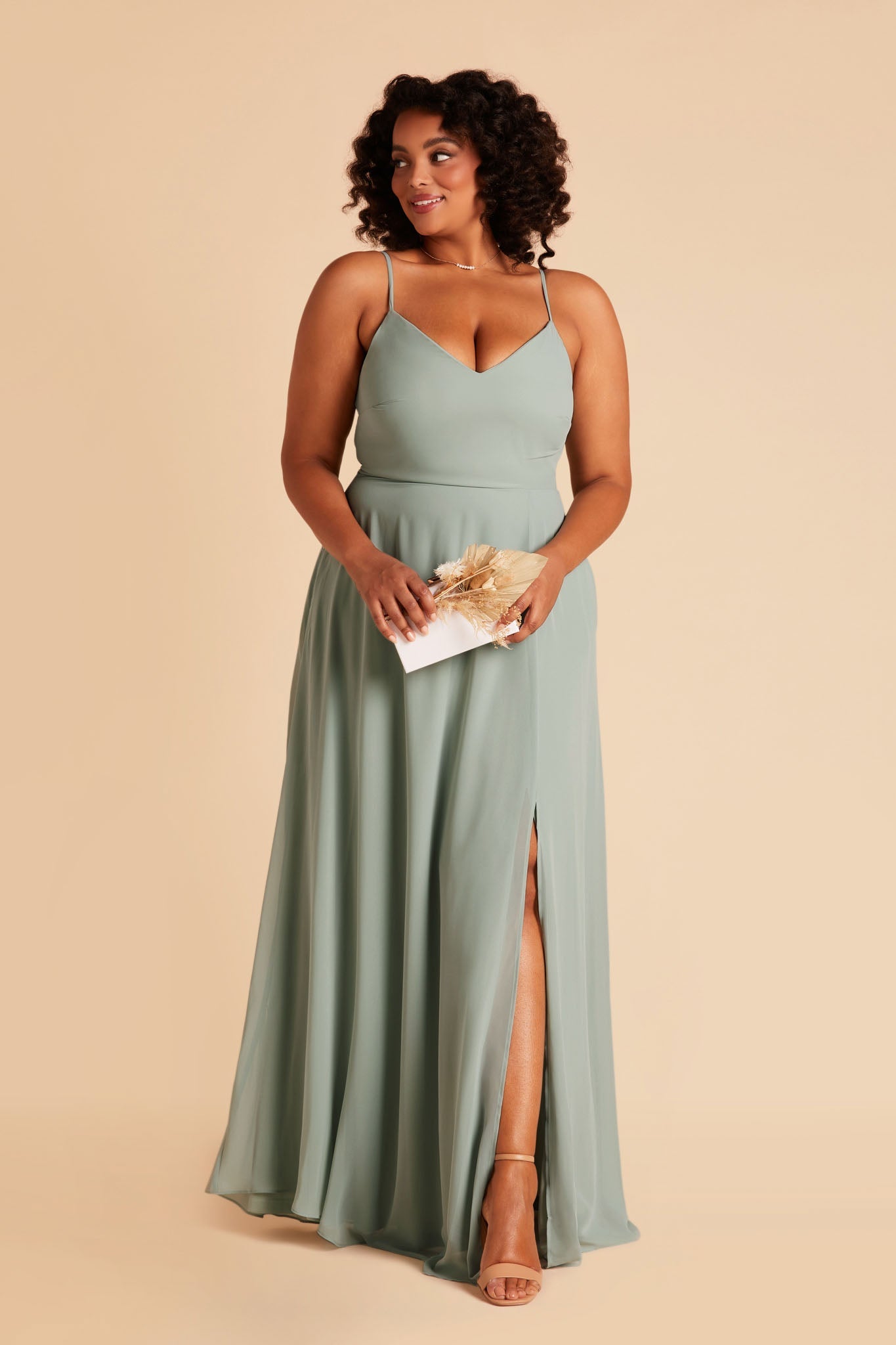 Front view of the floor-length Devin Convertible Plus Size Bridesmaid Dress in sage chiffon worn by a curvy model with a medium skin tone.