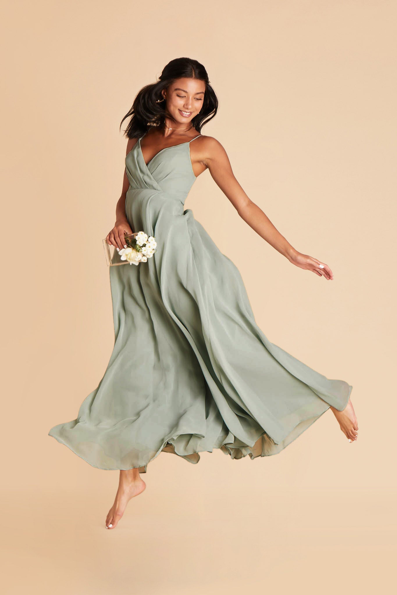 Front view of the Kaia Dress in sage chiffon shows the model in a low leap with the floor length skirt flowing around their feet.