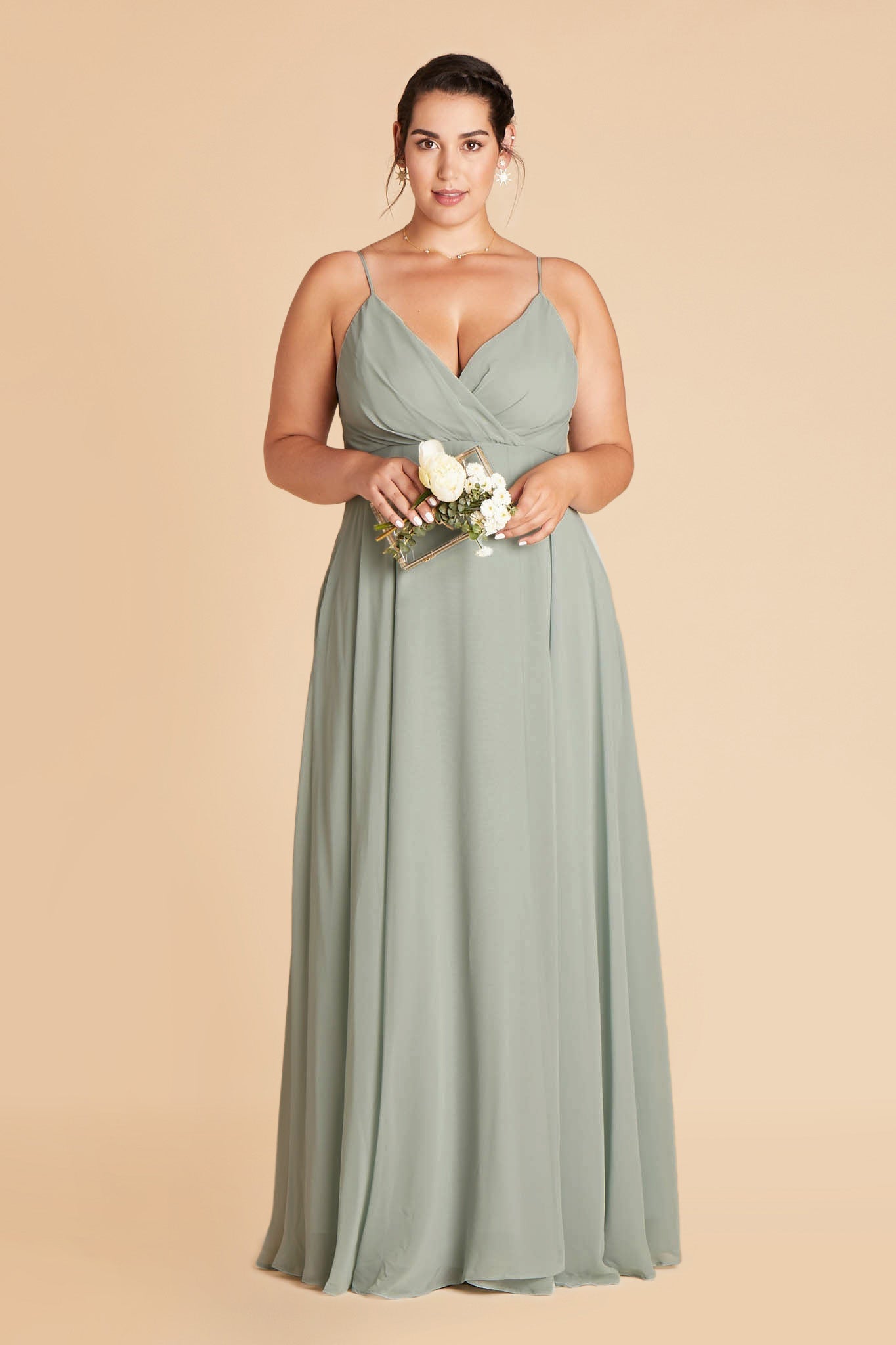 Front view of the floor-length Kaia Dress Curve in sage chiffon shows a full-figured model with a light skin tone wearing a spaghetti strap V-neck dress with a raised empire waistline wraps across their full bosom showing cleavage.